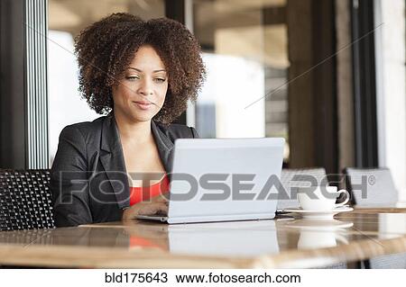 Stock Image - Mixed race businesswoman using laptop in cafe. Fotosearch