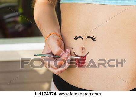 Picture - Mixed race girl painting face on stomach. Fotosearch