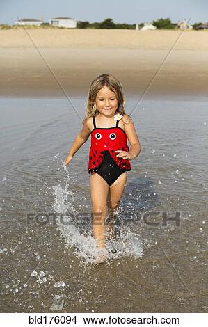 Picture - Mixed race girl splashing in waves on beach. Fotosearch