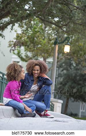 Stock Image - Mixed race mother and daughter sitting outdoors. Fotosearch