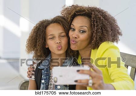 Stock Photography - Mixed race mother and daughter taking selfie. Fotosearch