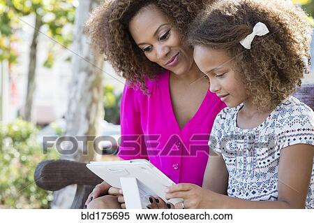 Stock Photography - Mixed race mother and daughter using digital tablet. Fotosearch