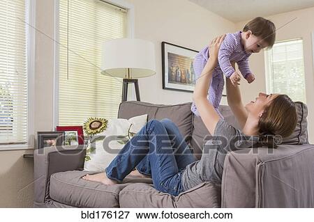 Stock Photo - Mixed race mother playing with baby daughter on sofa. Fotosearch