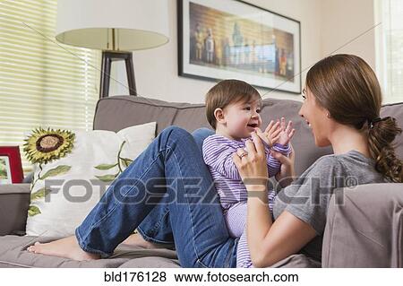 Stock Photo - Mixed race mother playing with baby daughter on sofa. Fotosearch