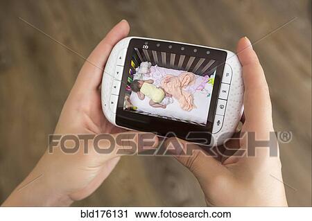 Stock Image - Mixed race mother watching baby monitor. Fotosearch
