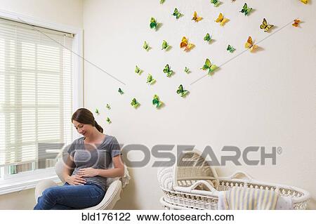 Stock Image - Mixed race pregnant woman sitting in nursery. Fotosearch