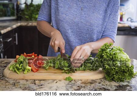 Stock Photograph - Mixed race woman chopping vegetables in kitchen. Fotosearch