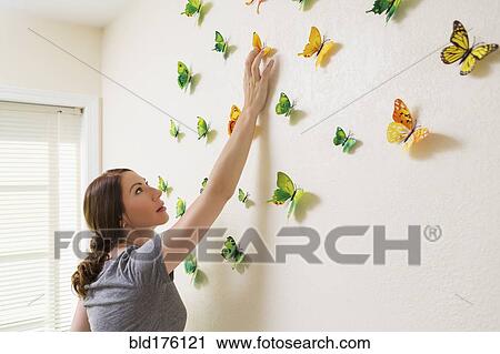 Stock Image - Mixed race woman decorating wall with butterflies. Fotosearch