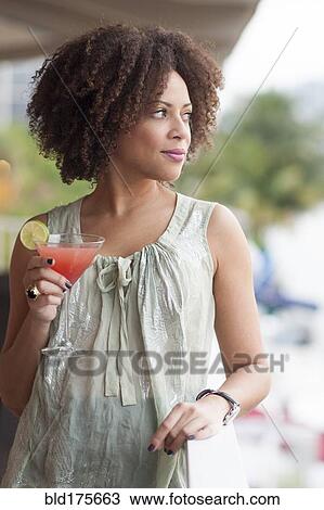Stock Image - Mixed race woman drinking cocktail on patio. Fotosearch