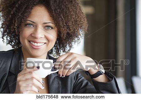 Stock Photo - Mixed race woman drinking coffee in cafe. Fotosearch