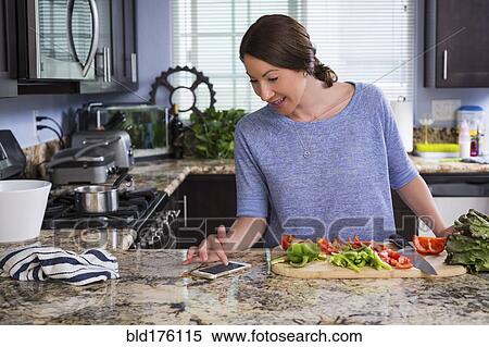 Stock Photography - Mixed race woman reading recipe on cell phone in kitchen. Fotosearch