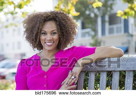 Stock Photograph - Mixed race woman smiling on bench. Fotosearch