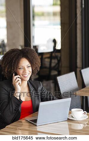 Stock Photography - Mixed race woman talking on cell phone in cafe. Fotosearch