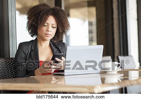 Picture - Mixed race woman using cell phone in cafe. Fotosearch
