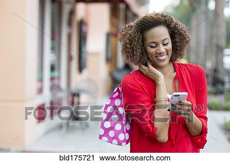 Stock Image - Mixed race woman using cell phone outdoors. Fotosearch