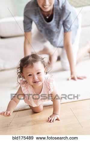 Stock Photo - Mother and baby daughter crawling in living room. Fotosearch