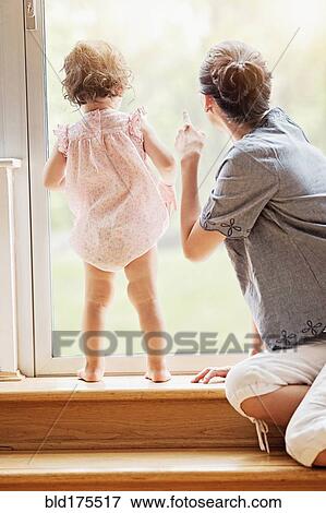 Stock Photo - Mother and baby daughter looking out window. Fotosearch