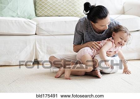 Stock Image - Mother and baby daughter playing in living room. Fotosearch