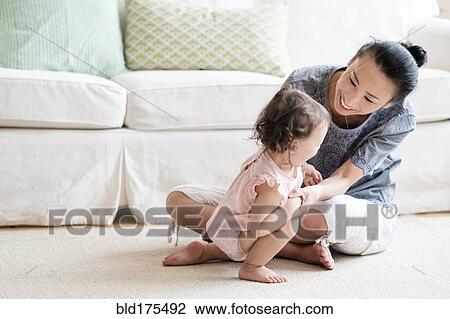 Mother and baby daughter playing in living room View Large Photo Image Stock Image - Mother and baby daughter playing in living room. Fotosearch