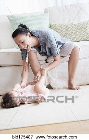 Stock Photo - Mother and baby daughter playing in living room. Fotosearch