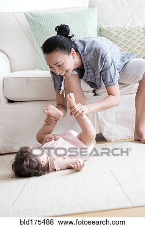 Stock Photo - Mother and baby daughter playing in living room. Fotosearch