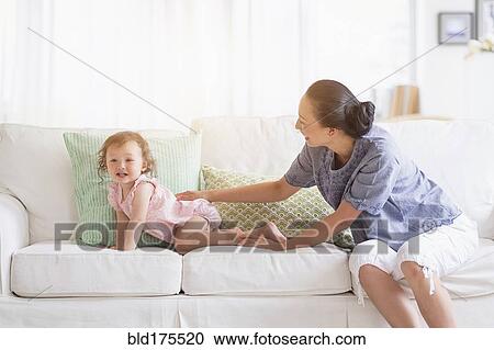 Stock Image - Mother and baby daughter playing on sofa. Fotosearch