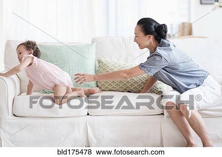 Stock Photo - Mother and baby daughter playing on sofa. Fotosearch