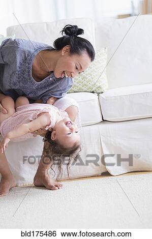 Stock Photograph - Mother and baby daughter playing on sofa. Fotosearch