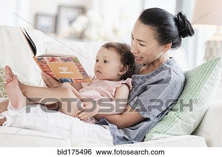 Stock Photograph - Mother and baby daughter reading on sofa. Fotosearch