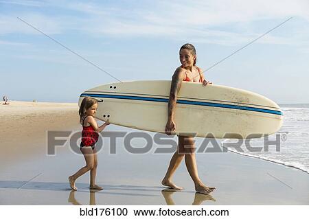 Mother and daughter carrying surfboard on beach View Large Photo Image Stock Image - Mother and daughter carrying surfboard on beach. Fotosearch