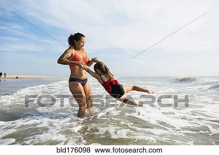 Stock Photo - Mother and daughter playing in waves on beach. Fotosearch