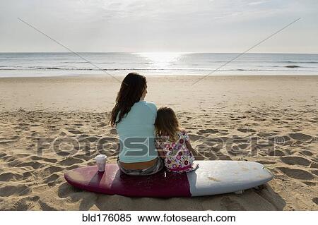 Stock Photography - Mother and daughter sitting on surfboard at beach. Fotosearch
