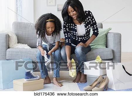 Stock Photograph - Mother and daughter trying on shoes on sofa. Fotosearch