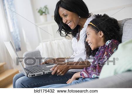Stock Image - Mother and daughter using laptop on sofa. Fotosearch