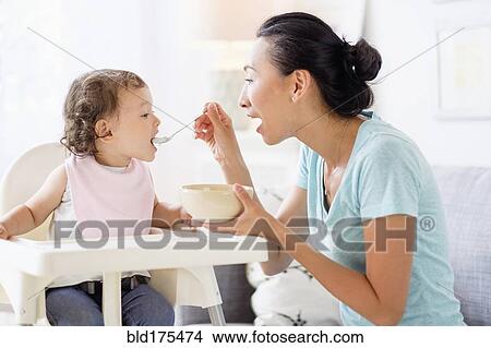 Mother feeding baby daughter in high chair View Large Photo Image Picture - Mother feeding baby daughter in high chair. Fotosearch
