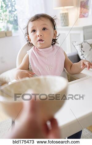 Stock Image - Mother feeding baby daughter in high chair. Fotosearch