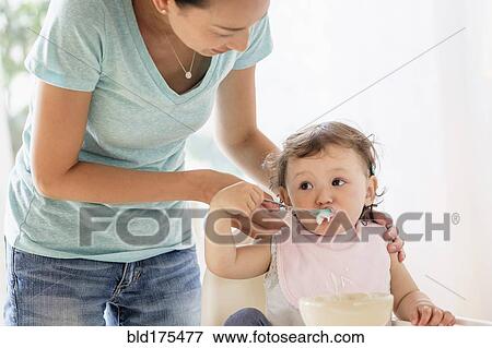 Mother feeding baby daughter in high chair View Large Photo Image Stock Photo - Mother feeding baby daughter in high chair. Fotosearch