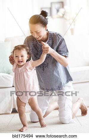 Picture - Mother helping baby daughter walk in living room. Fotosearch
