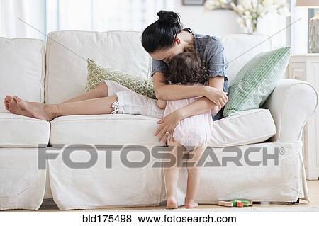 Stock Photo - Mother hugging baby daughter on sofa. Fotosearch