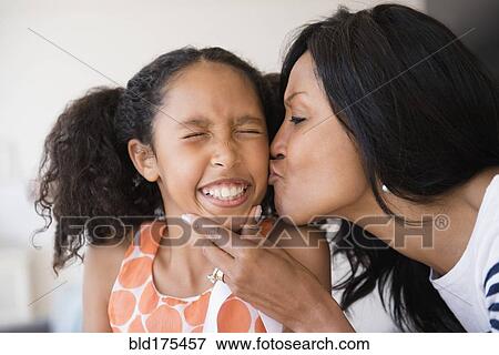 Stock Photo - Mother kissing cheek of squinting daughter. Fotosearch