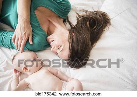 Stock Image - Mother laying with baby daughter. Fotosearch