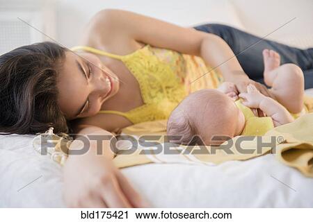 Stock Image - Mother playing with baby daughter on bed. Fotosearch
