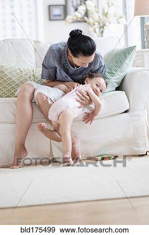 Stock Photo - Mother playing with baby daughter on sofa. Fotosearch