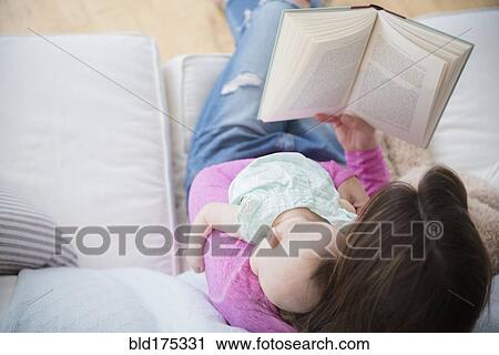Stock Image - Mother reading book and holding baby daughter. Fotosearch