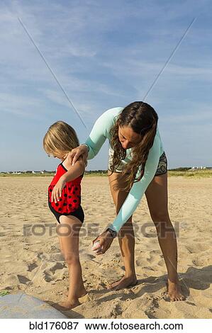 Stock Photo - Mother spraying sunscreen on daughter at beach. Fotosearch
