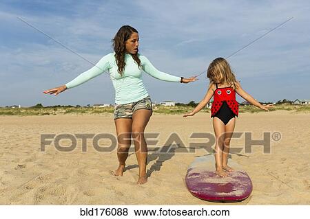 Stock Photo - Mother teaching daughter to surf at beach. Fotosearch