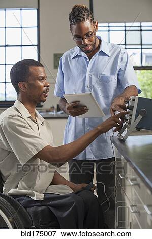 Stock Photo - Paraplegic student and classmate working in science classroom. Fotosearch