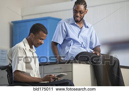 Stock Image - Paraplegic student and classmate using digital tablet. Fotosearch