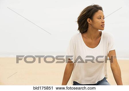 Stock Image - Pensive African American woman sitting at beach. Fotosearch
