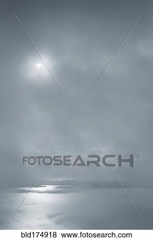 Stock Photo - Sun shining in cloudy sky over ocean. Fotosearch
